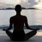 woman sitting cross-legged in yoga pose by ocean.