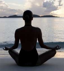 woman sitting cross-legged in yoga pose by ocean.